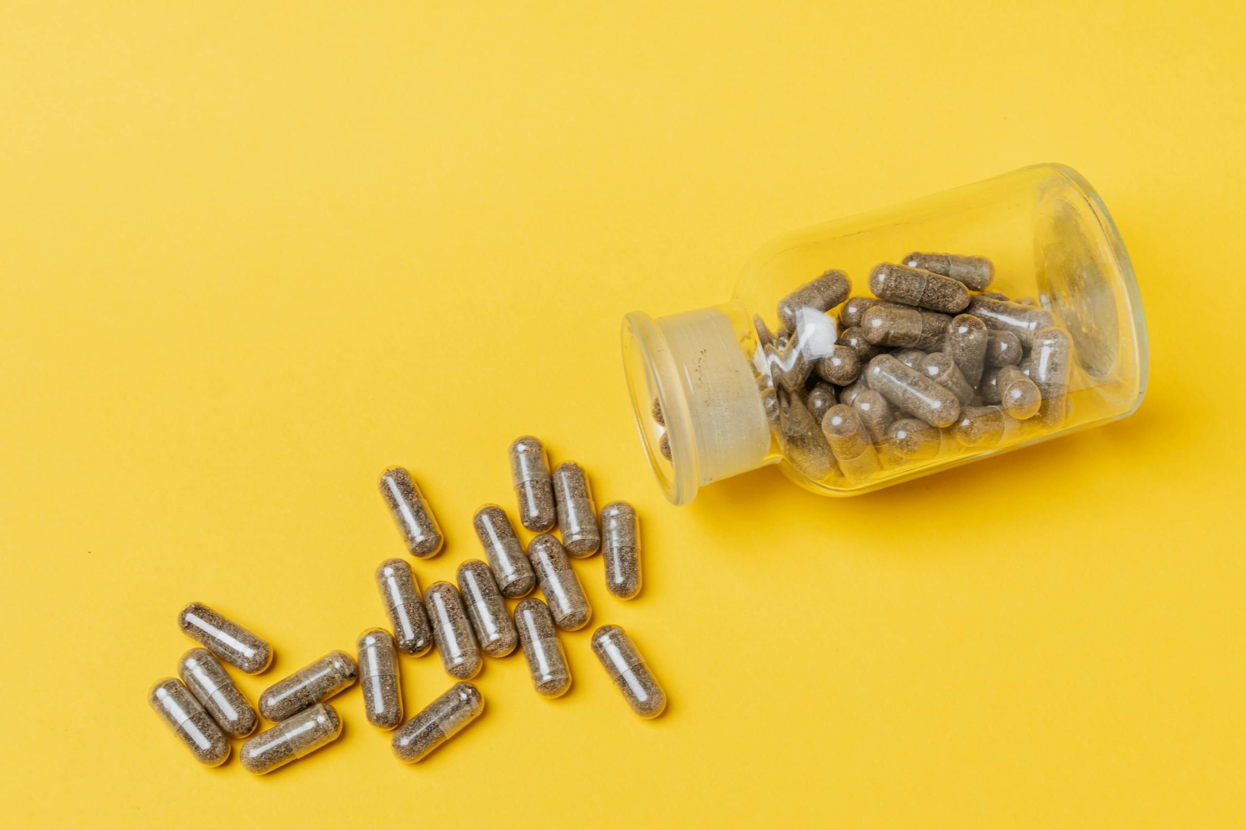 A glass bottle spilling capsules on a vivid yellow background. Perfect for healthcare and medicine themes.